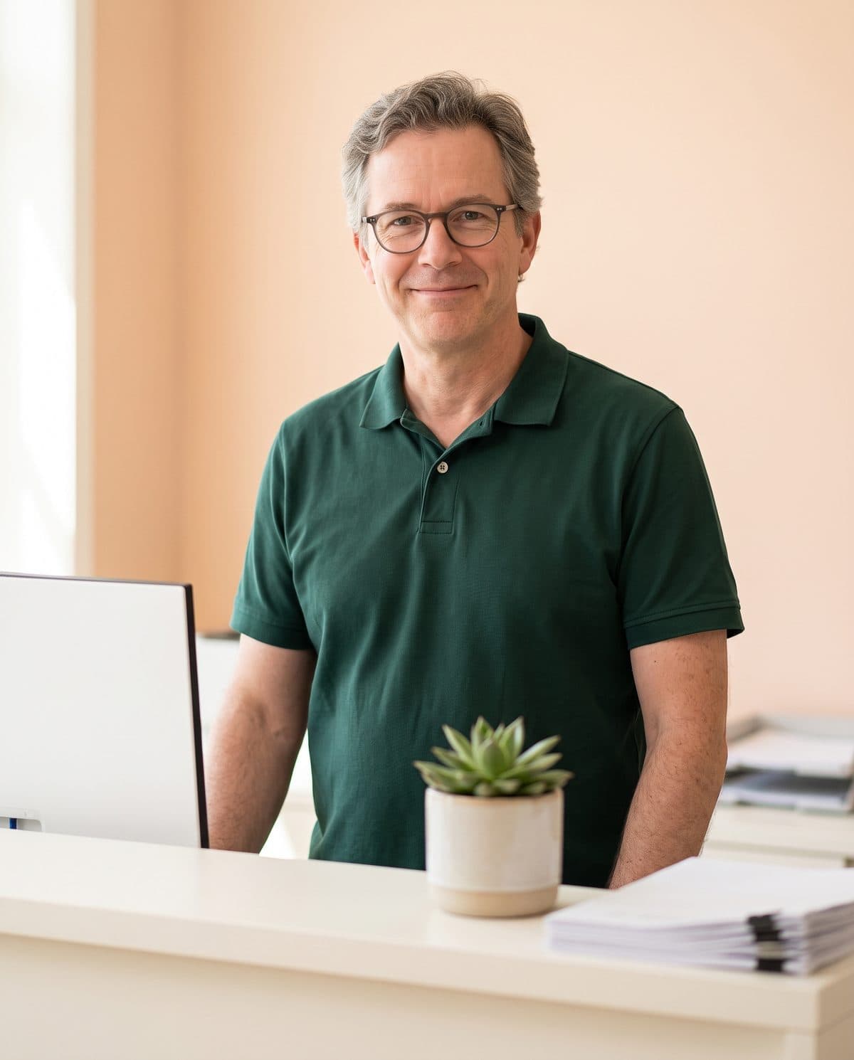 Tom Bradley, patient coordinator, at the front desk with a small succulent beside his monitor.